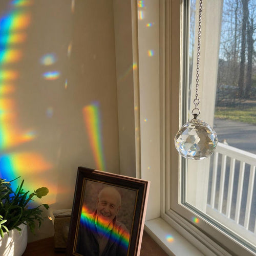 Crystal suncatcher in a sunny window casting a rainbow across a framed photo